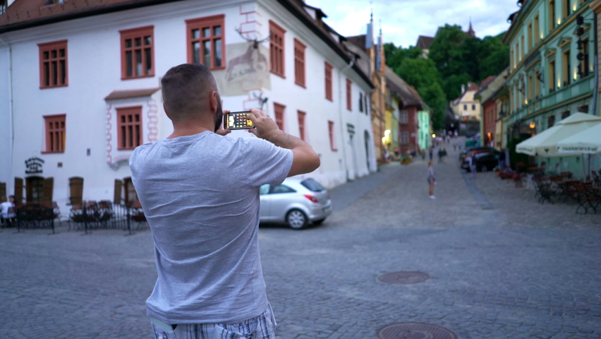 Young man taking photo with smartphone of old town in Romania