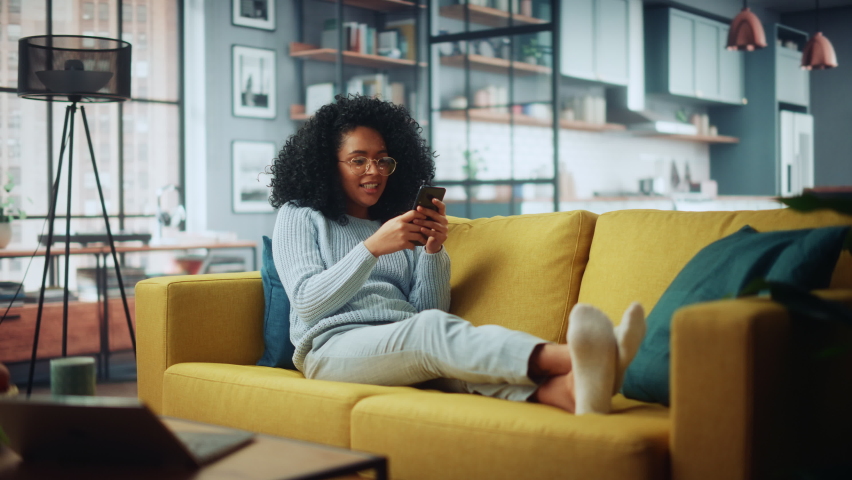 Happy Beautiful Latina Female Using Smartphone in Cozy Living Room at Home. Female Resting on Comfortable Sofa. She's Browsing the Internet and Checking Videos on Social Networks and Having Fun. Royalty-Free Stock Footage #1067430689