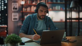 Handsome Caucasian Man With Headphones Talk on Video Conference Call on Laptop while Sitting in Dark Living Room in the Evening. Student Studying in Home School. Chat with Friends on Social Network.