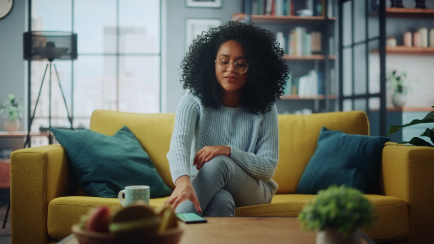Portrait of a Beautiful Authentic Latina Female in a Stylish Cozy Living Room Using Smartphone at Home. She's Browsing the Internet and Checking Videos on Social Networks and Having Fun. Royalty-Free Stock Footage #1067430944