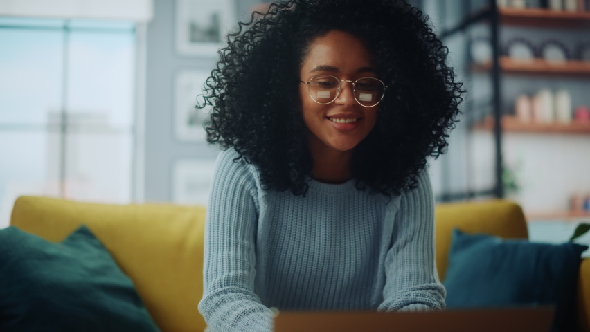 Close Up Portrait of a Beautiful Authentic Latina Female in a Cozy Living Room Using Laptop Computer at Home. She's Browsing the Internet and Checking Videos on Social Networks and Having Fun.
