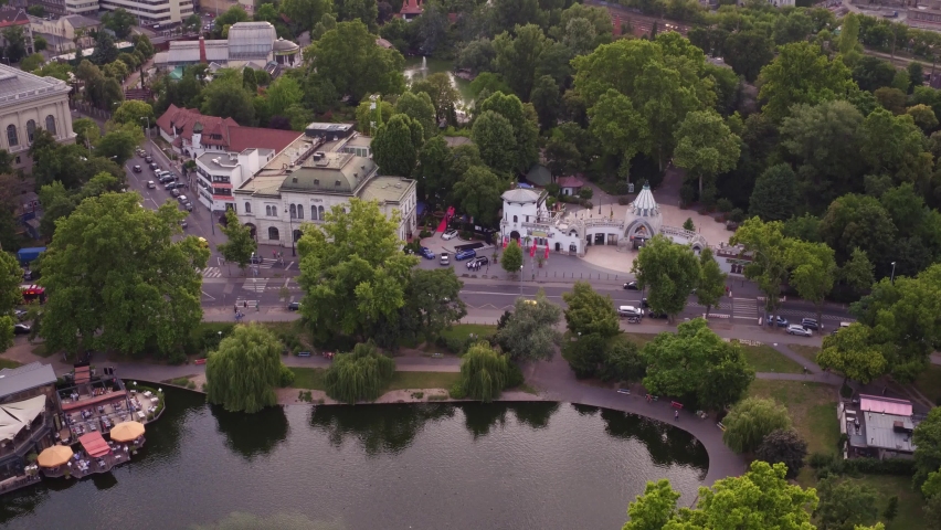 Aerial view of the Budapest city park in Hungary. In the background are the city buildings, in the foreground green foliage trees and the park lake on a summer afternoon. Cityscape and landscape.
