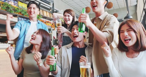 asian six friends watch ball games on tv and toasting beer in the restaurant