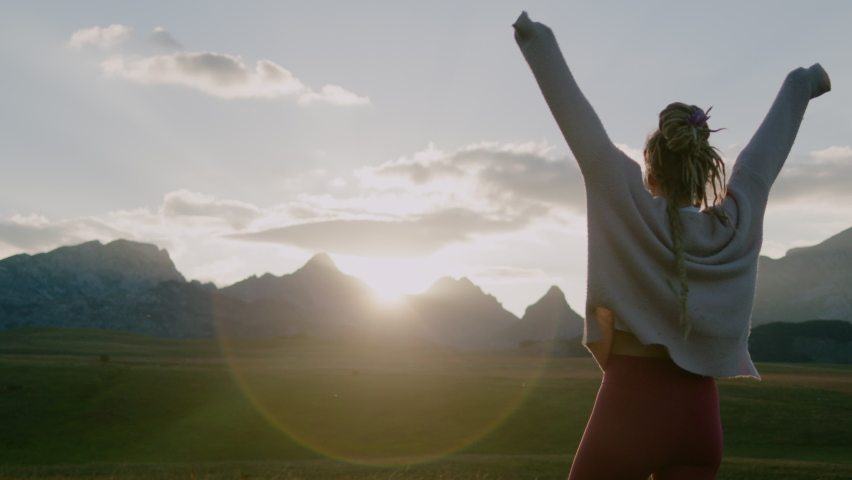 Happy woman with dreadlocks jumping and having fun in Field under sunlight in evening.  Enjoying summer and freedom, slow motion
