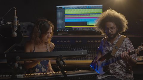Music studio. Sound recording. Afro man and hispanic woman recording in the sound studio. Brunette curly couple are playing guitar, keyboard and singing in comfortable environment.