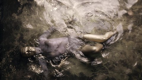 The woman is in the water lying on her back, covered all over with gold paint. Lies and poses beautifully.