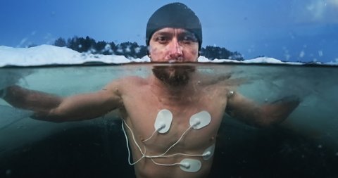 Medical test in the cold. Young man swims in the icy water with medical electrodes connected to his body and looks at the camera