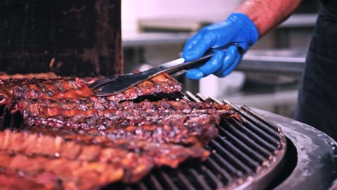 Barbecue Grilled Meat. Juicy Pork Ribs are Roasted on the Rotating Hot Grate of a Huge Barbecue Grill, the Chef Turns the Ribs with a Spatula.