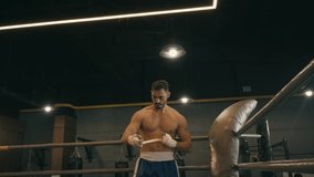 bearded hispanic boxer wrapping hands with boxing tape and exercising in gym