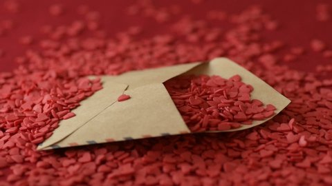 Red scarlet heart shaped sugar confetti crumbling and falling down in men's hands on red background. Romantic love, Saint Valentine's Day preparation design concept