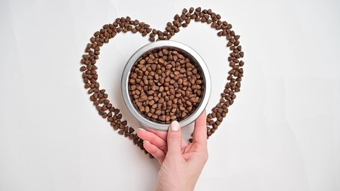 Dry food for dogs or cats flows down into a heart shape on a white backdrop. A woman puts a plate of food for pets