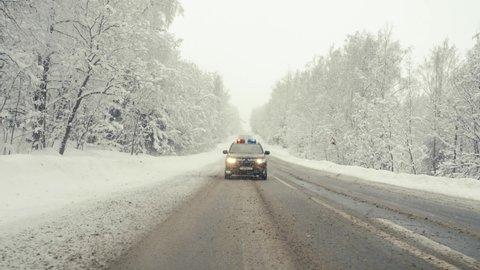 Cop car in high speed pursuit. Emergency response police patrol vehicle speeding to scene of crime. Heavy snowfall and fog on the road. Outdoor front view of police traffic auto driving. 
