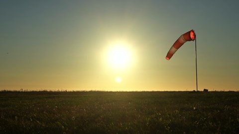 Windsock on blue sky. Red and white wind sock on th wind. Sun shines into lens. A small plane in the sky in the background