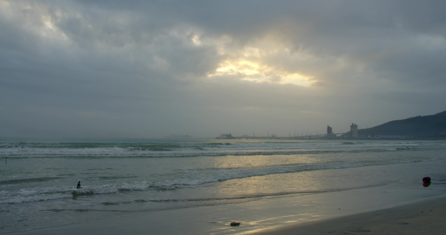 A large sun appears from behind the clouds, and large mountains touch the horizon and coast. Asian beach background. The trail of the sun on the waves in the sand.