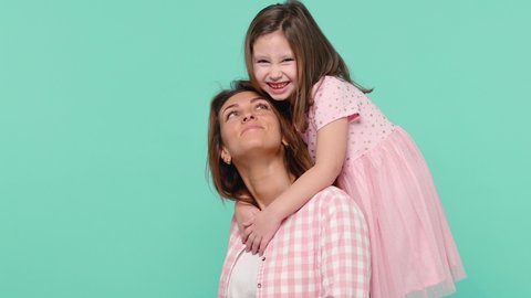 Happy woman in pink clothes have fun with cute child baby girl 5-6 years old. Mommy little kid daughter stand behind hug kiss isolated on pastel blue background studio Mother's Day love family concept