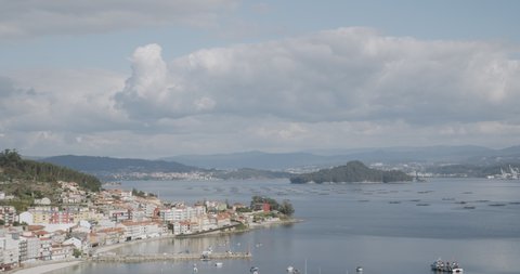 Camera tilt from traditional house to the panoramic view of Ria de Pontevedra, Galicia, Spain. Raxo town at foreground and Marin harbor at background on sunny day. Beautiful seascape of Galicia