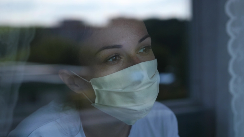 Young woman wears a mask to protect herself from covid-19 while looking out the window Royalty-Free Stock Footage #1067463383
