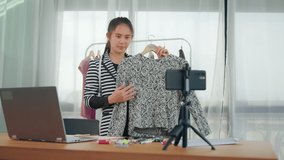 Asian sales business woman live stream video recording online social media marketing application, selling clothing fashion advertisement, using computer wireless smartphone technology home office.