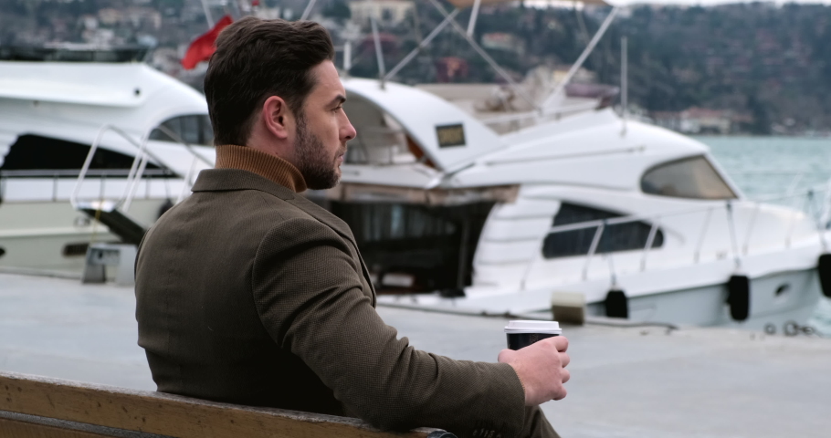 happy man enjoying turkish coffee on the shore of the pier with yachts, in the background the turkish flag. businessman on a coffee break between business meetings resting on the bench.istanbul,Turkey