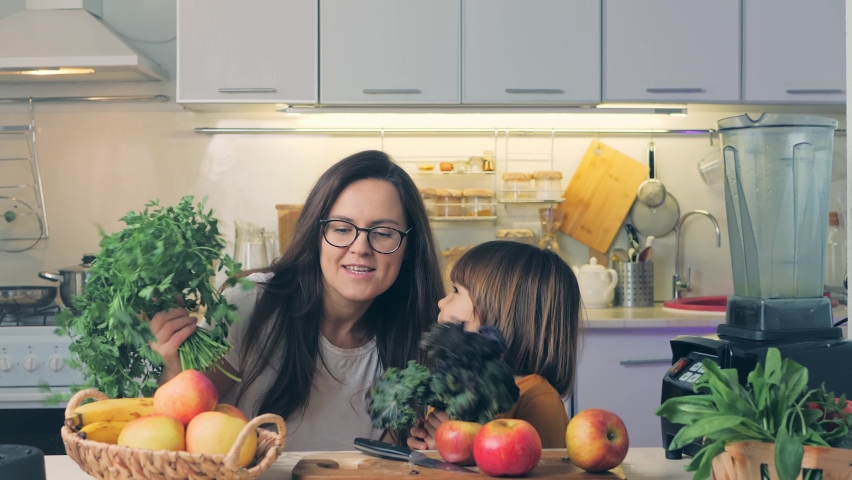 Funny young mom and child daughter making bunches fresh herbs having fun. Happy kid helping mum in kitchen laughing, play, dance. Cheerful vegan family enjoying cooking activity Royalty-Free Stock Footage #1067467712