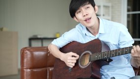 young Asian man playing guitar music and sing a song relax to record video live streaming, musician artist work from home, new normal lifestyle on cyberspace online communication