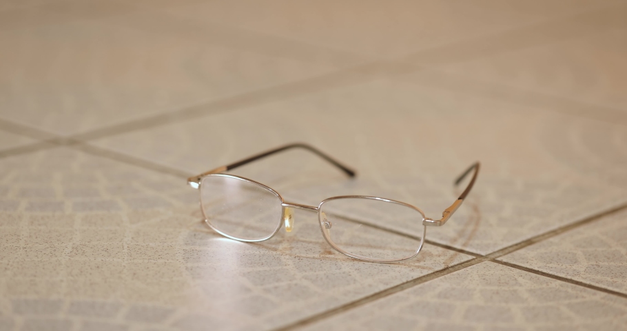 Stepping on reading glasses destroying them on the floor, picking up afterwards