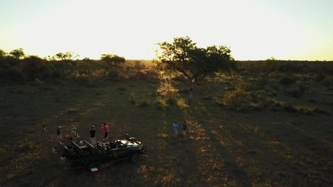 A stunning drone shot of a group of friends enjoying sundowners during a beautiful African sunset. Revealing the majesty of the African safari landscape.