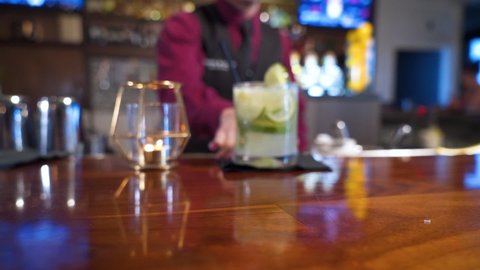 Bartender serves national drink of Brazil Caipirinha garnished with limes, slider close up slow motion 4K