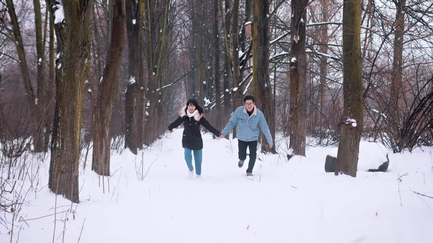 Childish happy couple running through the park covererd in snow and holding hands. Slow motion. High quality 4k footage