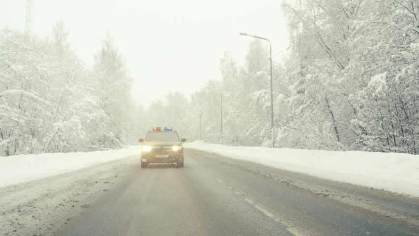 The police car chases the intruder in the day in a snowfall. Outdoor front view of police traffic auto driving. 