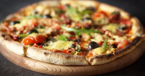 Fresh pizza with cheese, tomatoes, olives and arugula on a wooden board on a dark background.