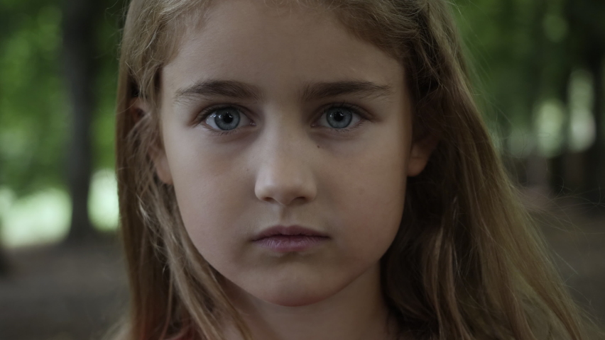 Portrait Little Child Girl Looking at Camera Standing on Street in City on Summer Day. Young Sad Thinking Curiosity Child Looking at Camera Closeup Outdoors. Face Eyes Serious Contemplative Child. | Shutterstock HD Video #1067487395