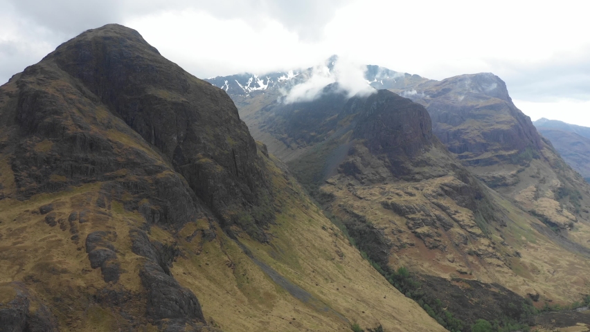 Aerial view of  highlands in Scotland, with clouds over the famous mountains known as Three Sisters of Glencoe - Moody weather in Scottish highlands - Background ready image of beautiful landscape