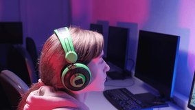 Young beautiful woman playing video games in the dark in big green headphones. 4k video. Blue and red light.