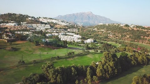 Aerial perspective of luxury urbanisations situated in Benahavís - Marbella area.  Private golf courses, expensive villas, luxury lifestyle. Drone forward and tilt down.  Spanish countryside 