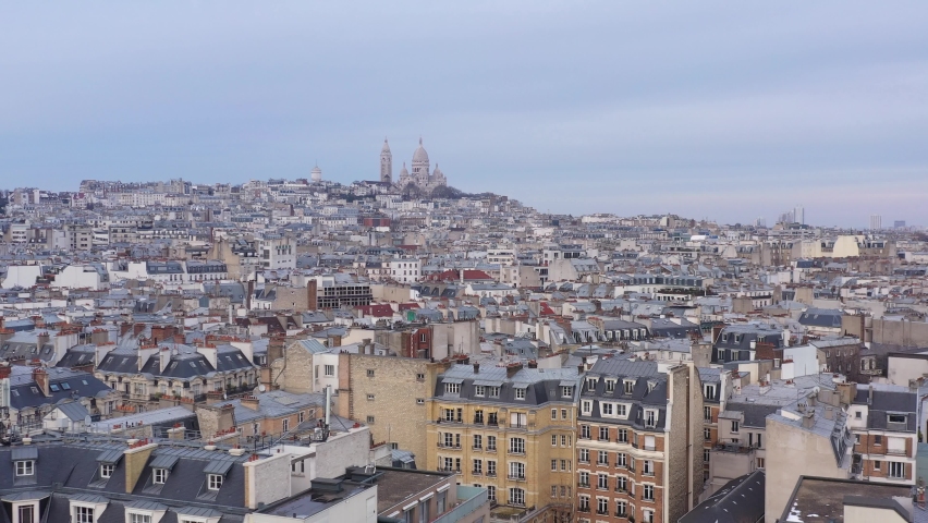 France, Paris, drone aerial view flying above buildings roofs with Sacré-Coeur Basilica church in the background. Pastel blue sky. Royalty-Free Stock Footage #1067494358