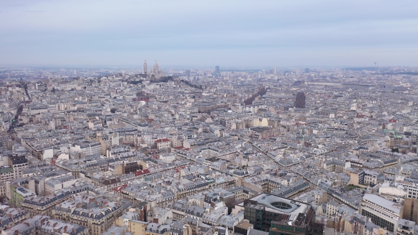 France, Paris, wide drone aerial view flying above buildings roofs with Sacré-Coeur Basilica church in the background. Pastel blue sky. Royalty-Free Stock Footage #1067494367