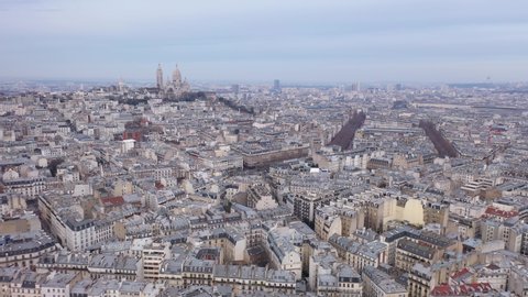 France, Paris, wide drone aerial view flying above buildings roofs with Sacré-Coeur Basilica church in the background. Pastel blue sky.