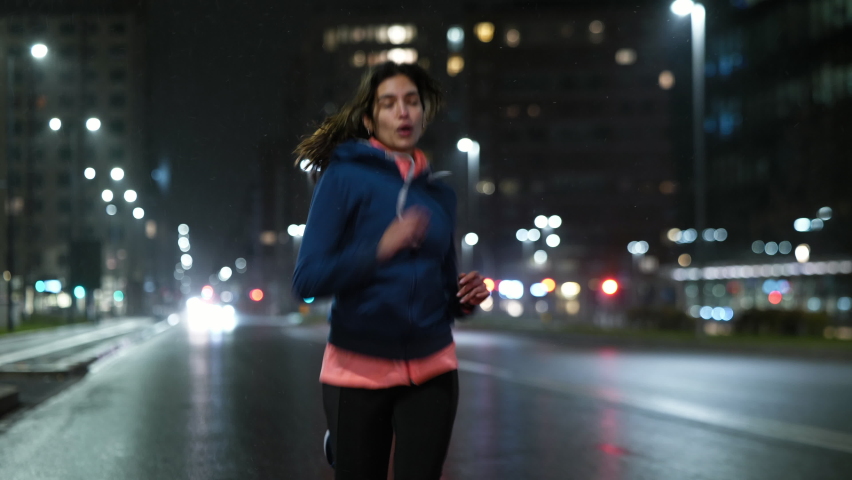 Cinematic shot of young arab sportswoman with athletic body is running with effort and dedication in city center with snow falling at night. Concept of determination, woman power and goal achievement. Royalty-Free Stock Footage #1067495756