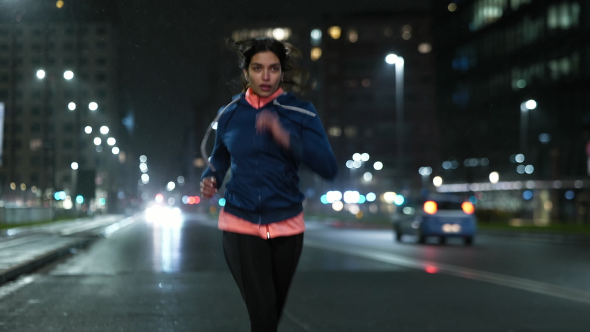 Cinematic shot of young arab sportswoman with athletic body is running with effort and dedication in city center with snow falling at night. Concept of determination, woman power and goal achievement. | Shutterstock HD Video #1067495756