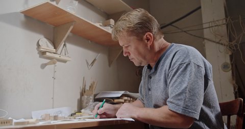 Craftsman creates a drawing project for a new product for children Eco toy cars sitting draws in his cozy little workshop during quarantine runs his small business