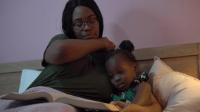 african american mother reading a book to her little daughter in bed before going to sleep at home. black mom story telling to girl in bedroom. sleepy child in parent embrace . kid with bedtime  - Powered by Shutterstock - Get 15% off with code: PIKWIZARD15