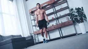 tilt view of shirtless sportsman squatting with dumbbells at home