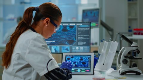 Scientist using digital tablet working in modern medical research laboratory, analyzing DNA information. Medicine, biotechnology research in advanced pharma lab, examining virus evolution