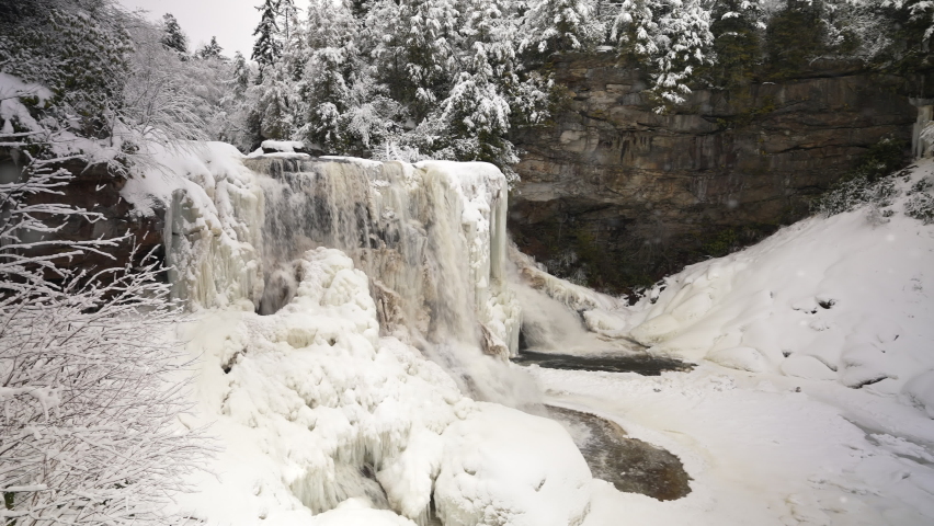 Blackwater Falls in state park in Davis, West Virginia in the winter with snow and ice panning to left showing icicles.
