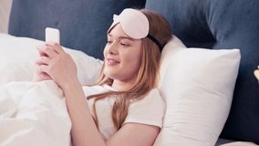 Young woman lying in bed and holding smartphone