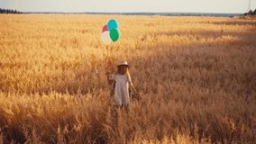 girl in white dress and straw hat walking with colorful balloons in wheat field