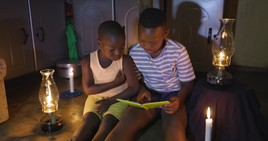 Poverty. Inequality. Poor young rural Black African children from an informal settlement slum try to do school work by candlelight and oil lamp in their tin shack home Royalty-Free Stock Footage #1067511635
