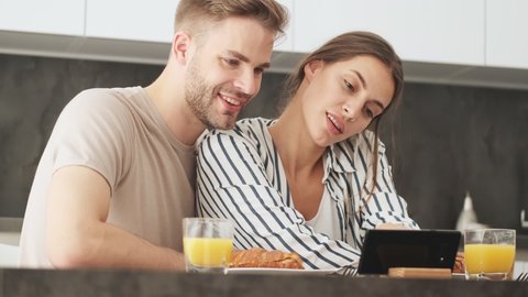 A good-looking young couple man and woman are sitting and watching video during breakfast in the kitchen at home