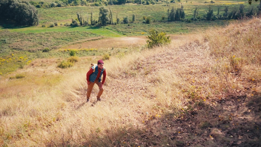 Traveler with backpack climbing up the hill at daytime